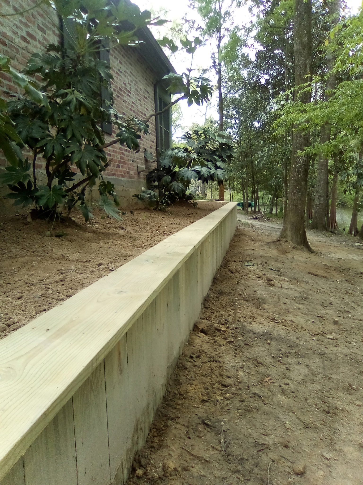 Treated timber retaining wall holding a graded slope beside a brick Louisiana home