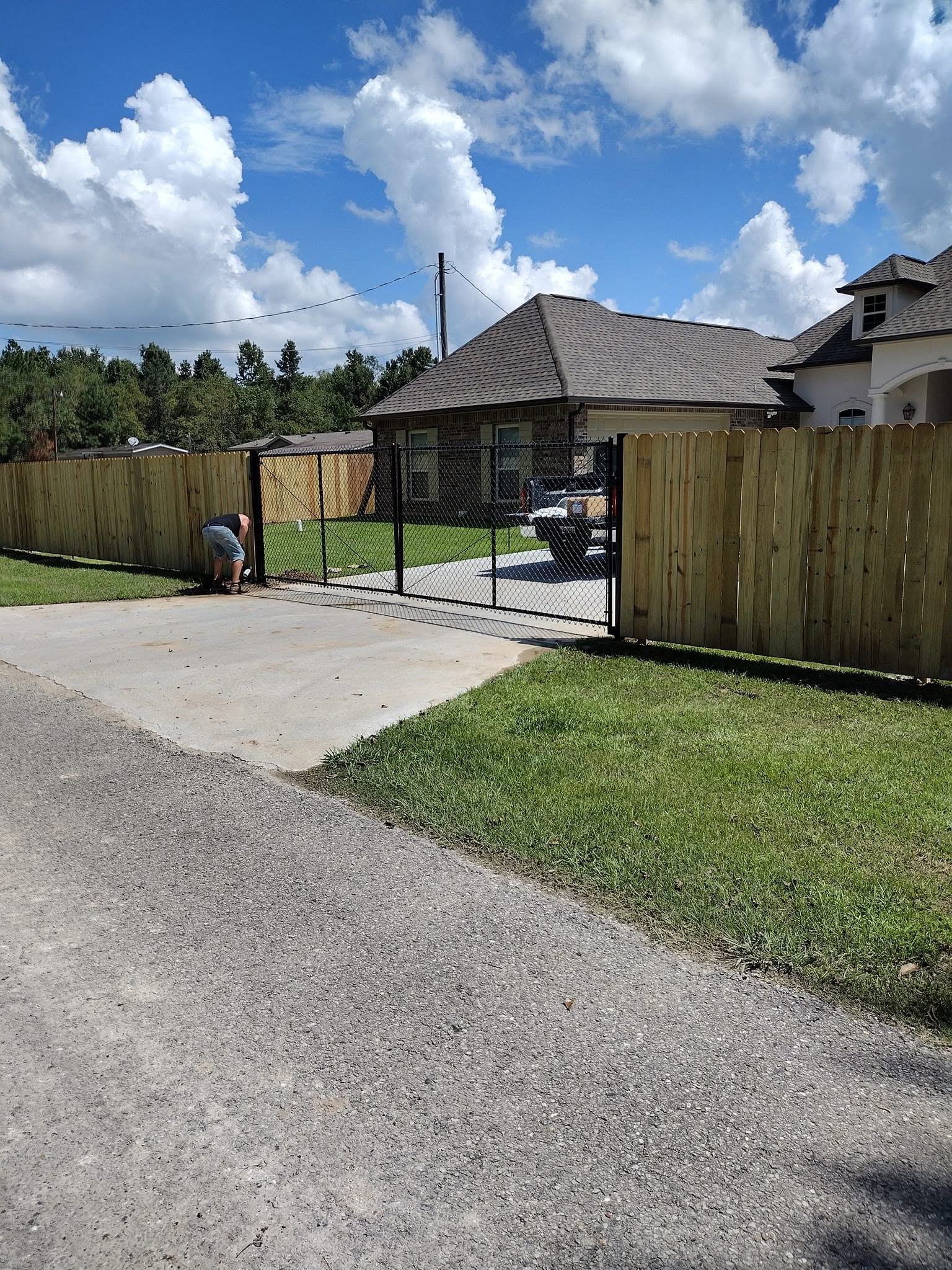 Wood privacy fence with a black chain link rolling driveway gate at a Louisiana home