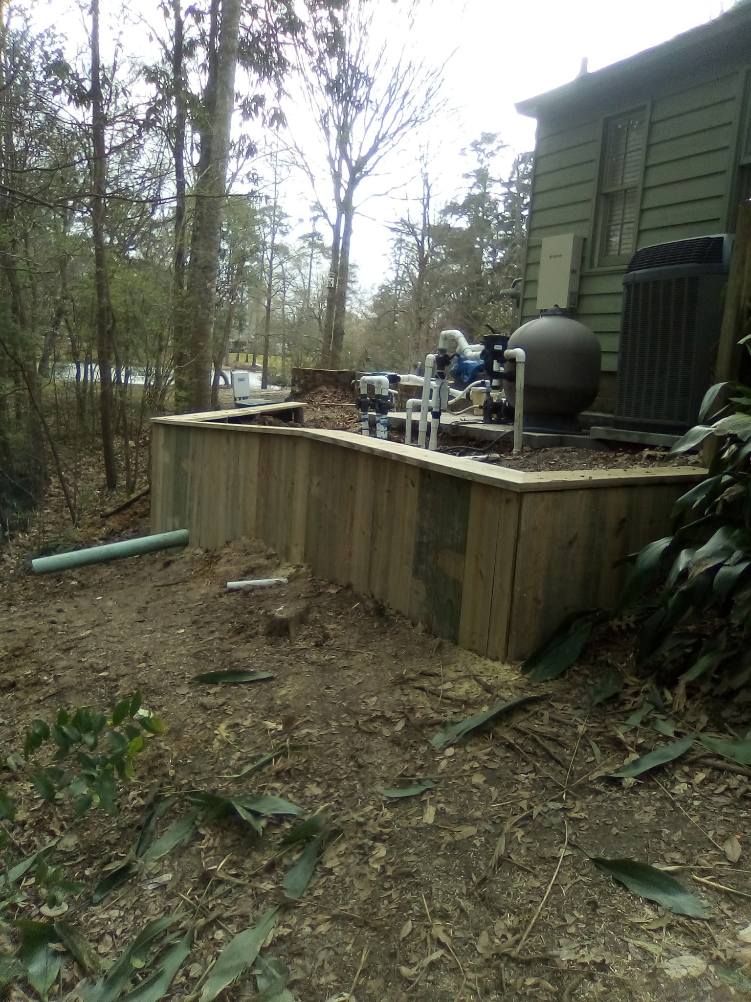 Low wood retaining wall creating a level pad for pool equipment at a Louisiana home